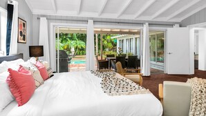 Une chambre spacieuse avec un grand lit, un ventilateur de plafond et une vue sur une piscine et un espace de détente extérieur.
