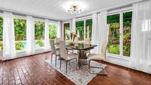 Un espace repas avec une table en verre, des chaises blanches et une vue sur une piscine et un jardin luxuriant.