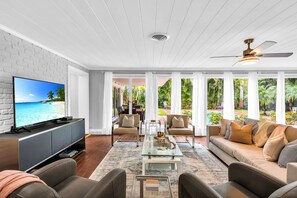 Una sala de estar con televisor, sofá, mesa de centro y vistas a un jardín.