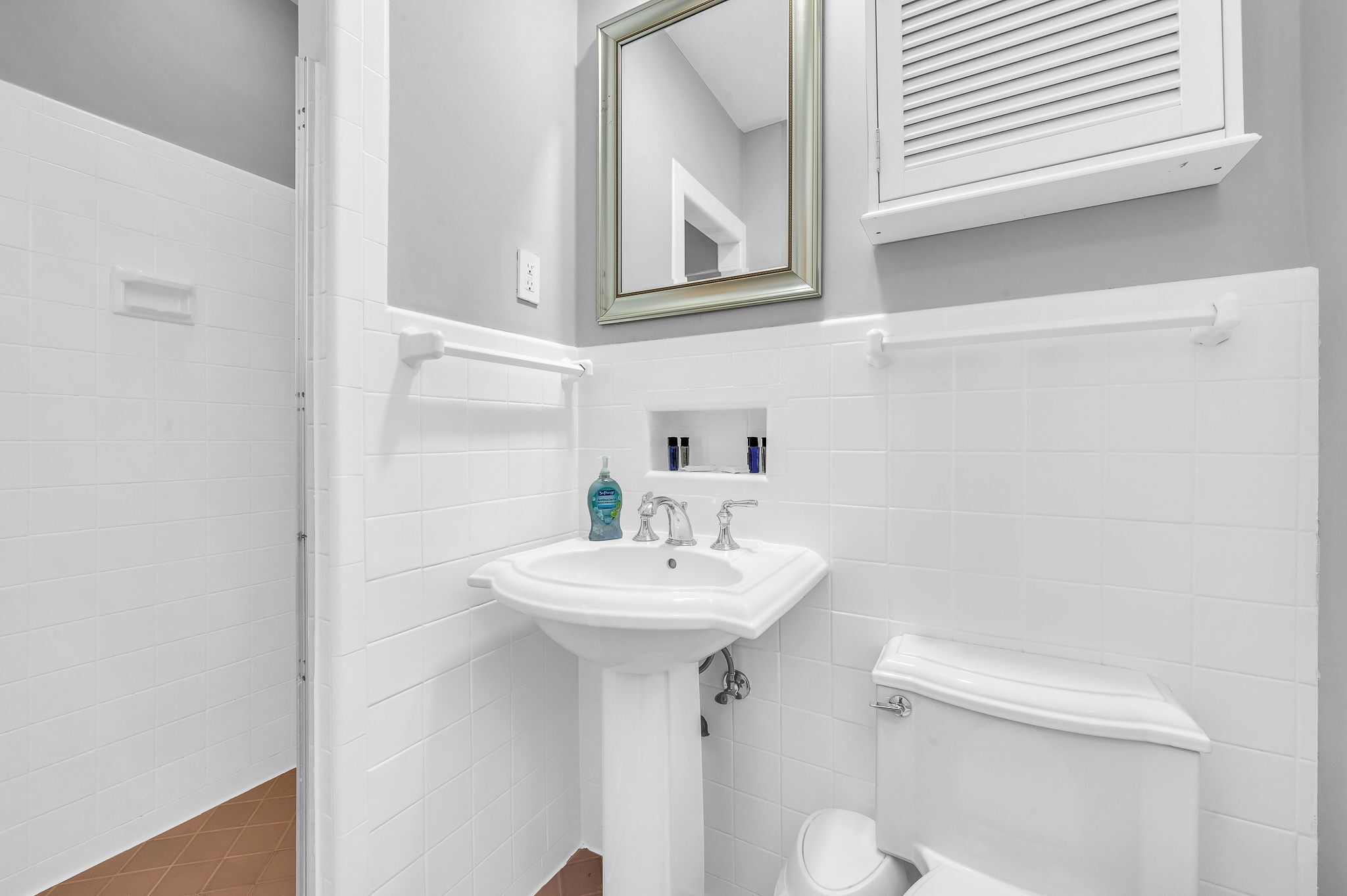 A bathroom with white tiles, a sink, a toilet, and a mirror.