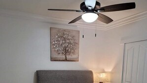 Ein Schlafzimmer mit einem Bett, einem Sessel, einem Deckenventilator, einer Lampe und einer Tür.