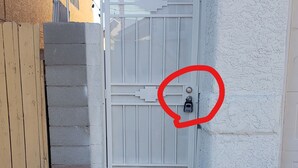 Ein verschlossenes Tor mit einem Metallgitter, einer Betonmauer und einem gepflasterten Weg.