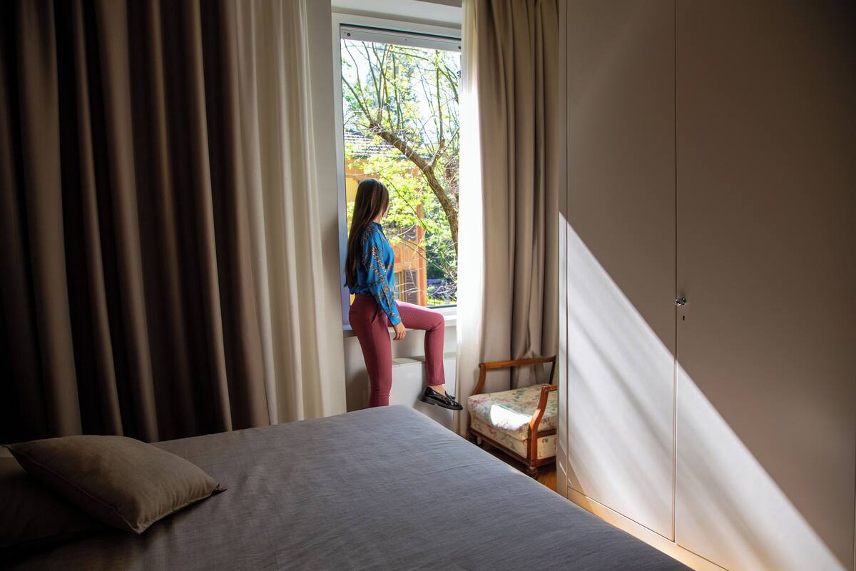 Quarto com cama, uma cadeira e janela com cortinas.