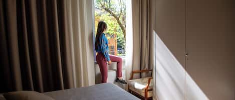 A bedroom with a bed, a chair, and a window with curtains.