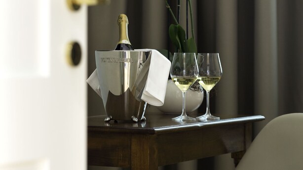 A table with a champagne bottle, two wine glasses, and a vase with white flowers. - Villaggio Narrante - Foresteria Delle Vigne (Serralunga d'Alba)