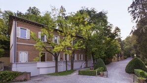 A brick building with white shutters, a cobblestone driveway, and neatly trimmed hedges. - Villaggio Narrante - Foresteria Delle Vigne (Serralunga d'Alba)