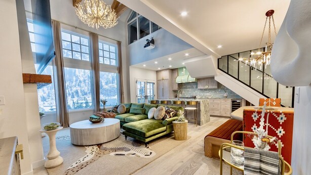 A spacious living area with a green sofa, a round coffee table, and a dining table with chairs. There is a staircase leading to an upper level. - 4 Bedroom WOW w/heated floors, Ski out access to Snowbird and steam bath. (Alta)