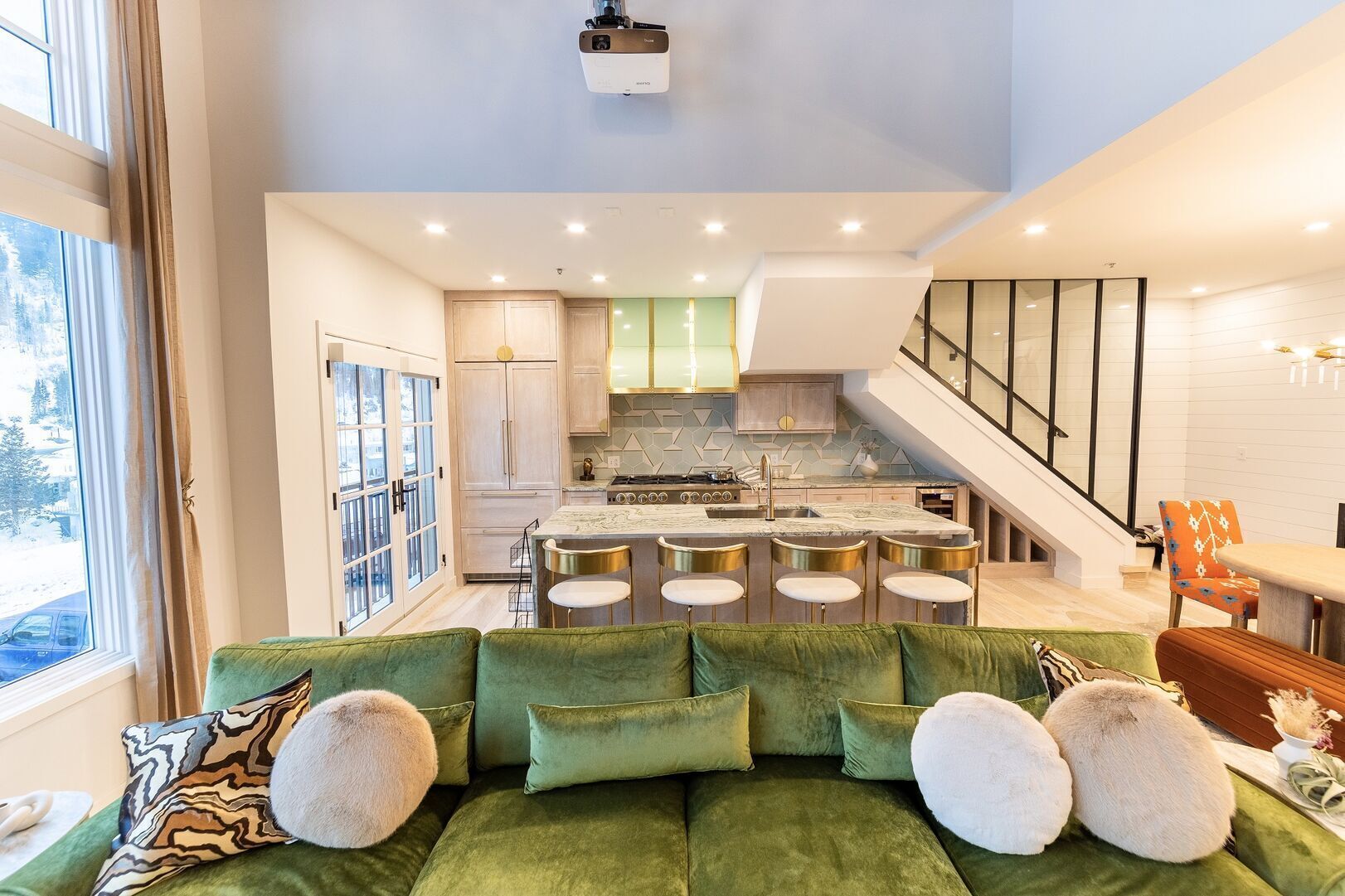 Une cuisine moderne avec un îlot central, un coin repas avec un escalier, et un canapé vert agrémenté de coussins décoratifs.