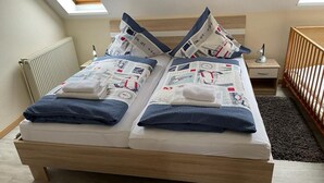 A twin bed with matching pillows, a bedside table, a nightstand, a wooden headboard, a radiator, a window with a view, and a wooden floor. - Vacation home "Sömmerwind 2 " Norddeich (Norden)