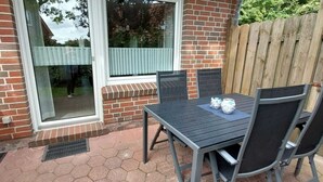 A patio with a table and chairs, a window, and a brick wall. - Vacation home "Sömmerwind 2 " Norddeich (Norden)