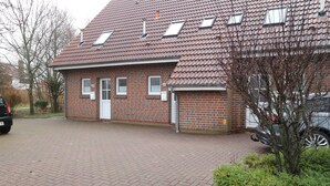 A red-brick building with a tiled roof, a paved driveway, and a small garden area. - Vacation home "Sömmerwind 2 " Norddeich (Norden)