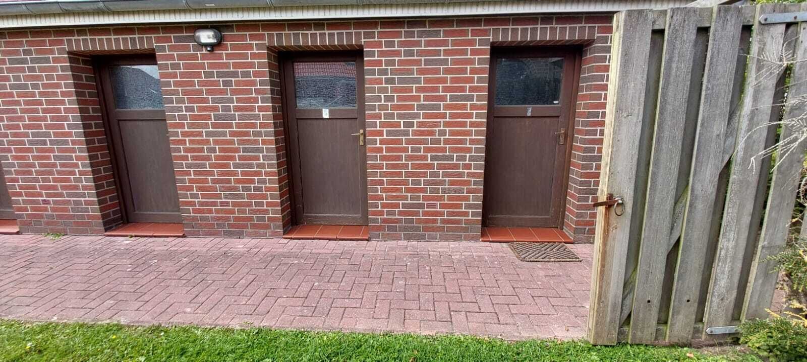 A brick building with three doors and a wooden fence.