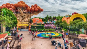 A theme park with a large tree structure, colorful attractions, and a central circular area with water features. - Gardaland House (Ronchi)