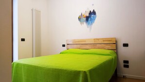 A bedroom with a wooden headboard, a green bedspread, and a wall painting of a mountain landscape. - Gardaland House (Ronchi)