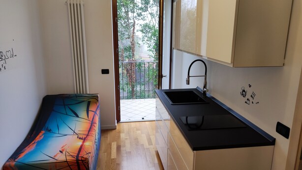 A compact kitchen with a black countertop, a sink, and a window overlooking a balcony. - Gardaland House (Ronchi)