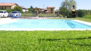 A rectangular swimming pool with a clear blue water surface, surrounded by a well-maintained grassy area. - Gardaland House (Ronchi)