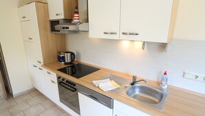 A compact kitchen with a stove, dishwasher, sink, and a microwave. - Vacation home "Sömmerwind 4" Norddeich, Riedeweg 12 (Norden)