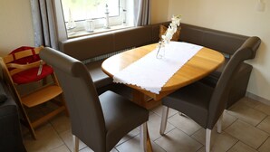 A dining area with a round wooden table, two brown chairs, a bench, and a window with curtains. - Vacation home "Sömmerwind 4" Norddeich, Riedeweg 12 (Norden)