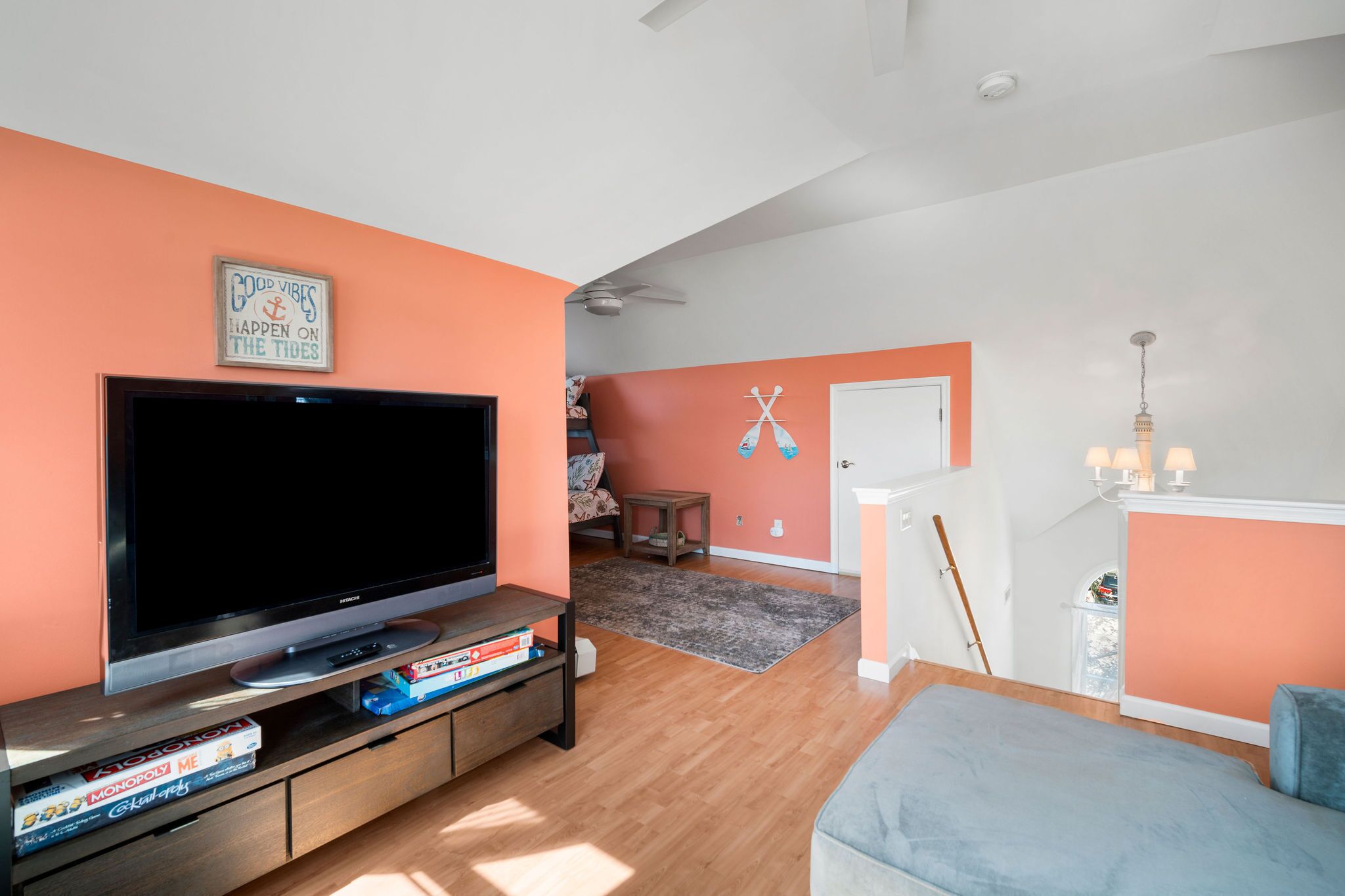 A living room with a flat-screen TV, a bookshelf with board games, a ceiling fan, and a door leading to another room.