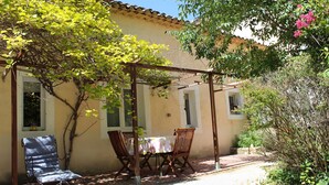 Eine Terrasse mit Tisch und Stühlen, einer Pergola und einem Gebäude mit Fenstern.