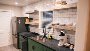 Una cocina moderna con gabinetes verdes, un refrigerador de acero inoxidable, un lavamanos doble y una ventana con persianas.