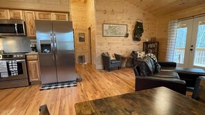 Eine moderne Küche mit Edelstahlgeräten, ein Essbereich mit einem Holztisch und eine gemütliche Sitzecke inklusive Sofa und Sesseln.