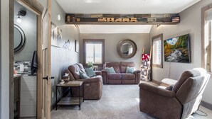 A cozy living room with a fireplace, leather sofas, a coffee table, and a large window with a view of the outdoors. - Pet Friendly Home! Cub House,3Br/2½Ba,Sleeps 8,Firepit,BBQ,Golf,20m 2 YNP (Island Park)
