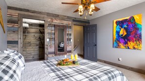 A bedroom with a bed, a ceiling fan, a wooden door, and a colorful painting. - Pet Friendly Home! Cub House,3Br/2½Ba,Sleeps 8,Firepit,BBQ,Golf,20m 2 YNP (Island Park)