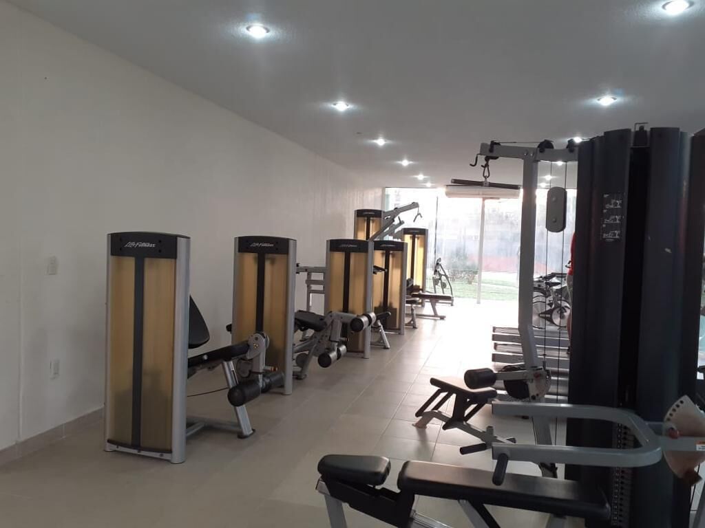 Een fitnessruimte met diverse trainingsapparaten, banken en een spiegelwand.