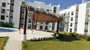 A modern hotel with a pool, a covered outdoor area with a thatched roof, and a well-maintained lawn. - Rent New Apartment in Acapulco 5 min. from the airport beach and La Isla. (Acapulco de Juárez)
