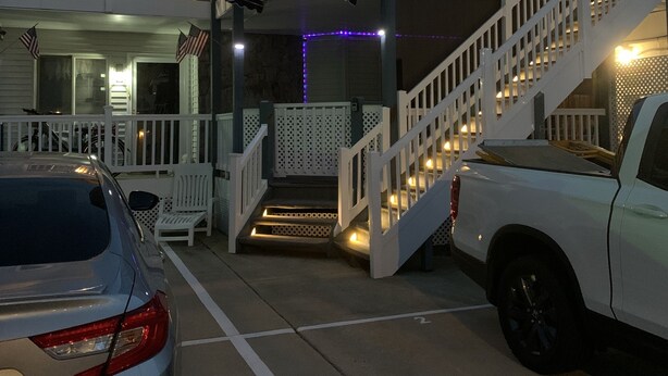 A two-story building with a balcony, a staircase, and a car parked in front.