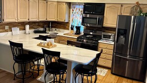 A modern kitchen with wooden cabinets, a central island with chairs, a stainless steel refrigerator, and a ceiling fan.