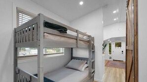 A bunk bed room with a window, a door, and a wooden floor.