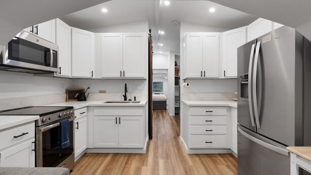 A modern kitchen with white cabinetry, stainless steel appliances, and a wooden floor.