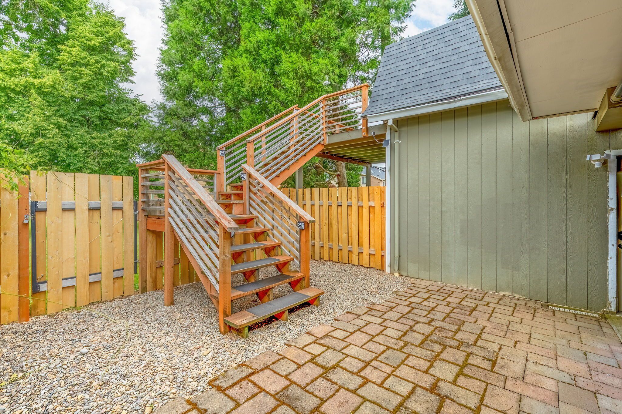 A wooden outdoor staircase leading to a covered area, surrounded by a wooden fence and gravel.