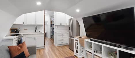 A compact living space with a kitchenette, a sofa, a TV, and a patterned rug.