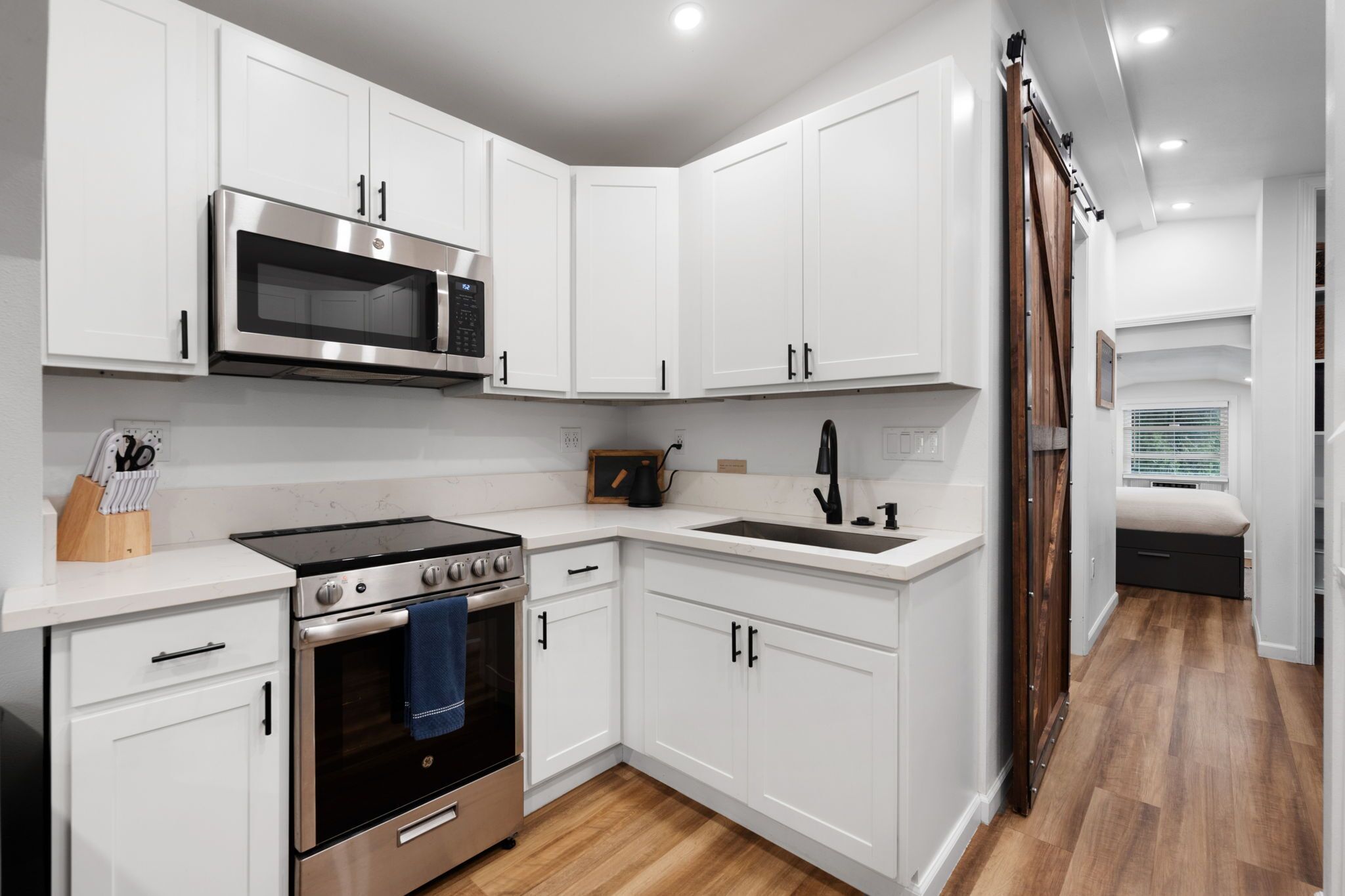 A modern kitchen with white cabinetry, stainless steel appliances, and a wooden floor.