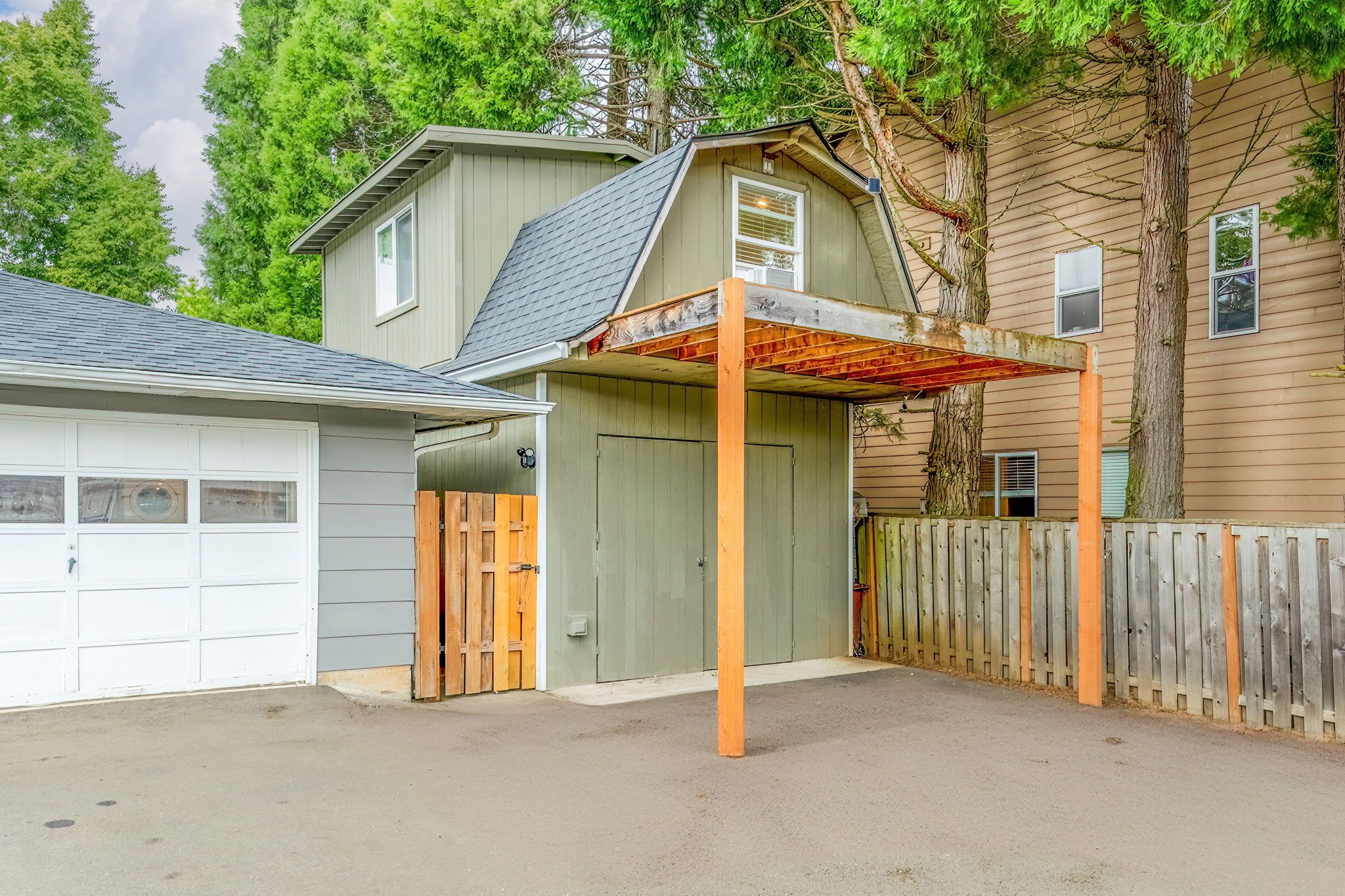 Un garage attenant à une maison, doté d’un porche couvert, d’une clôture en bois et d’une porte de garage.