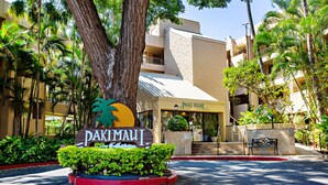 Entrada de hotel com uma placa indicando "Paki Maui", cercada por vegetação exuberante e palmeiras.
