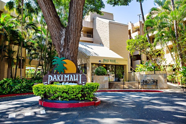 Entrada de hotel con un letrero que dice "Paki Maui", rodeada de exuberante vegetación y palmeras.