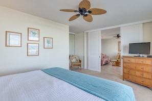 Un dormitorio con una cama, un aparador, un televisor y un ventilador de techo.