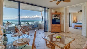 Uma varanda espaçosa com vista desobstruída para o oceano, um espaço de jantar com mesa de vidro e uma sala de estar com TV e assentos confortáveis.