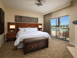 Relax in comfort with a large bed under a ceiling fan, surrounded by a view of palm trees and a clear sky.