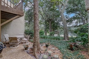 Un espace patio aménagé avec du mobilier d’extérieur, une terrasse en bois et un jardin agrémenté de diverses plantes et d’un petit élément décoratif aquatique.