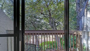 A balcony with two chairs and a wooden railing, overlooking a garden with trees and shrubs.