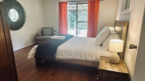 Ein Schlafzimmer mit Bett, Nachttisch mit Lampe, Stuhl und einem fenster mit Vorhängen.