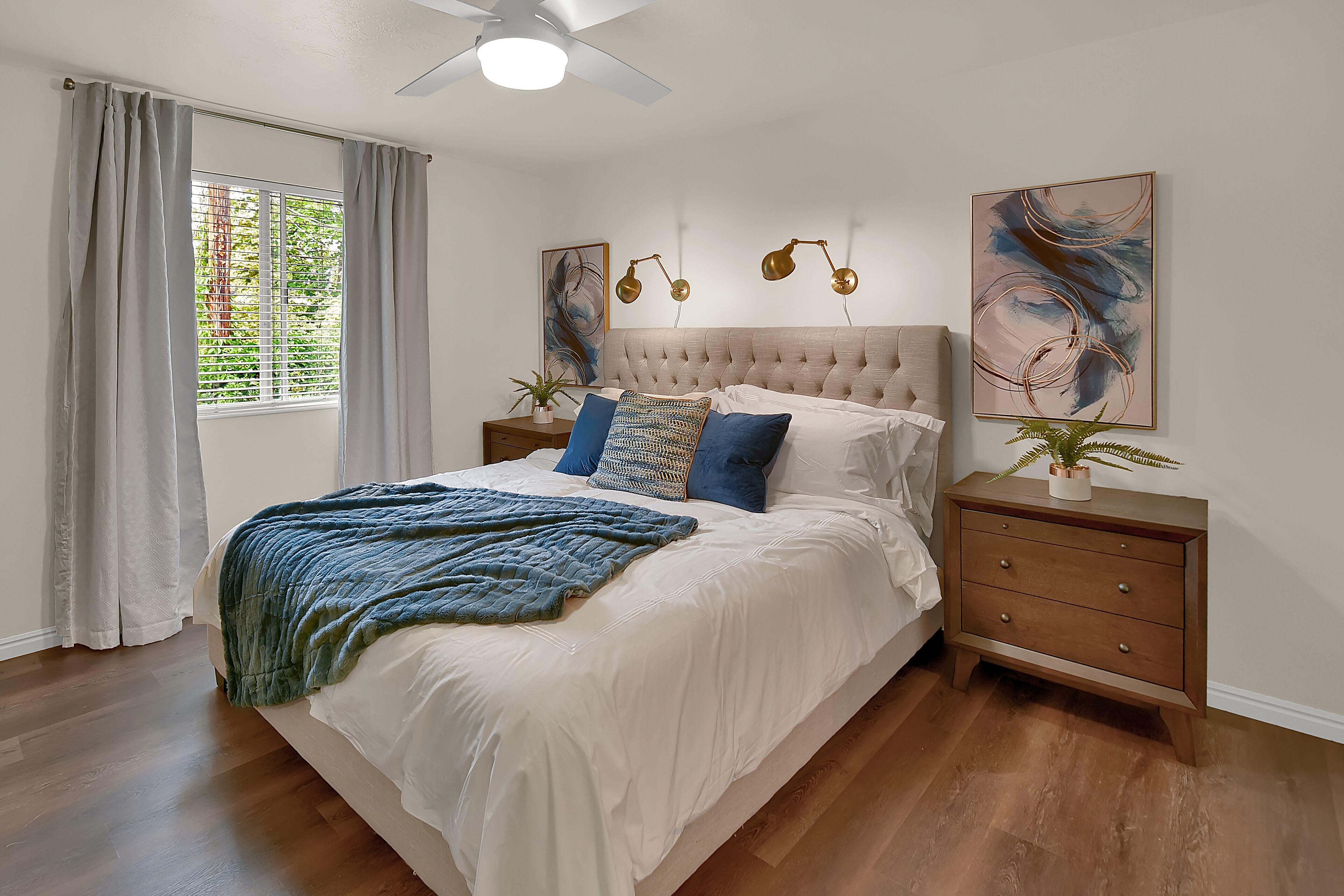 A bedroom with a tufted headboard, a large bed with white bedding, two bedside tables with lamps, and artwork on the walls.
