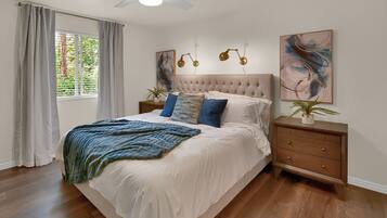 A bedroom with a tufted headboard, a large bed with white bedding, two bedside tables with lamps, and artwork on the walls.