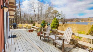 A wooden deck with chairs and a grill, overlooking a lake and trees. - Lakefront Cottage w Fireplace, Private Lake Access, Dock, Big Yard (Albrightsville)