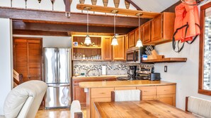 A compact kitchen with wooden cabinets, a stainless steel refrigerator, and a wooden dining table with chairs. - Lakefront Cottage w Fireplace, Private Lake Access, Dock, Big Yard (Albrightsville)